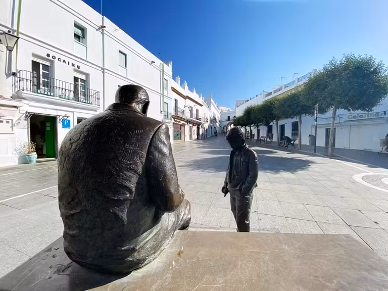 estatua en la plaza de españa de Conil con la puerta de la villa al fondo